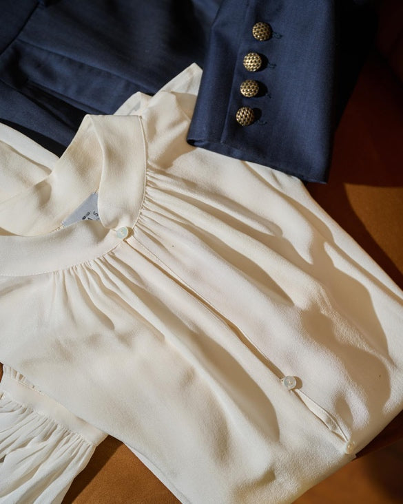 Una blusa di seta panna accanto a un blazer blu, in atelier